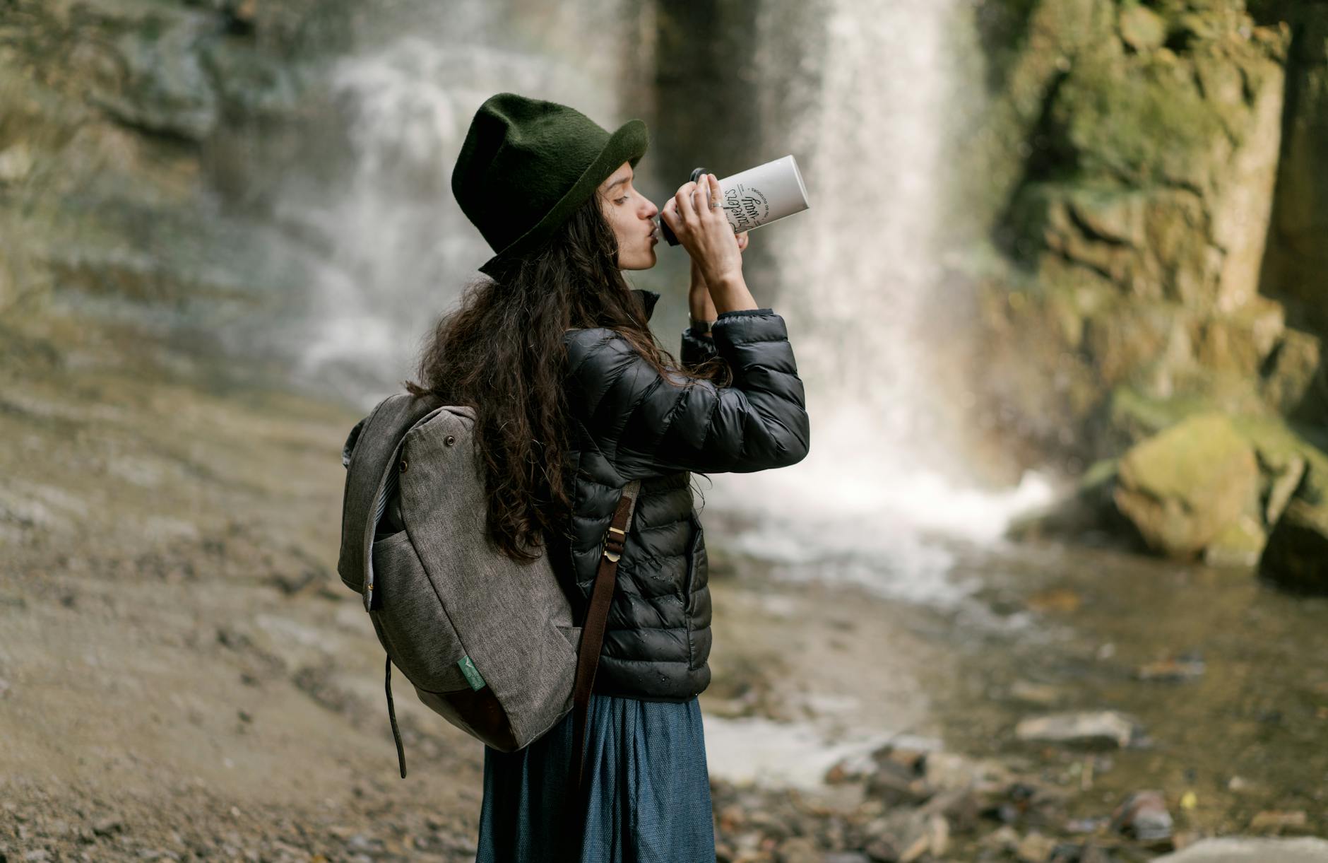 Girl standing by waterfall drinking out of a tumbler